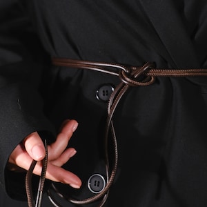 May include: A black blazer with a brown leather belt tied in a knot at the waist. The belt is long enough to be tied in a bow.