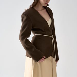 May include: A dark brown blazer with a V-neck design and a cream-colored belt. The blazer is paired with a long, beige skirt. The outfit is simple and elegant, suitable for various occasions.