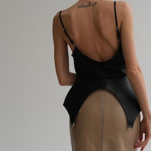 Peut inclure: Un haut de camisole noir et une ceinture en cuir noire sur une jupe crayon beige. Le dos de la personne est visible, avec un tatouage sur le haut du dos. La jupe a une fermeture éclair pleine longueur.