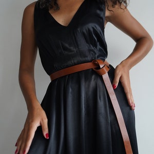 May include: A black sleeveless dress with a brown leather belt tied in a knot at the front.