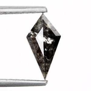 May include: A black diamond with a kite shape and a pointed tip. The diamond is held by tweezers against a white background.
