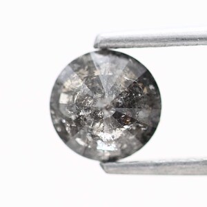 May include: A round, gray diamond with a faceted cut. The diamond is held in place by a pair of tweezers.