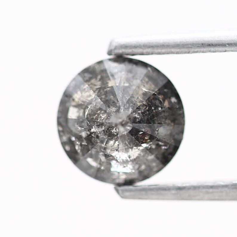 May include: A round, gray diamond with a faceted cut. The diamond is held in place by a pair of tweezers.