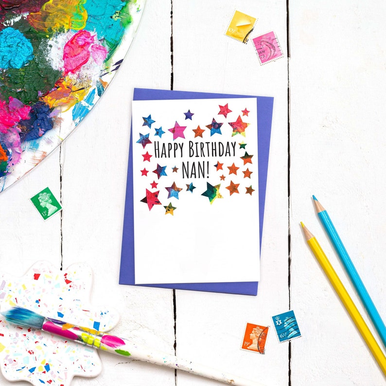 May include: A white card with a purple envelope. The card has a colorful star design and the text "Happy Birthday Nan!"