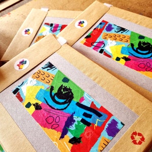 May include: Four brown paper envelopes with colorful abstract designs printed on the front. The designs feature geometric shapes, lines, and a black cat silhouette. The envelopes have a white sticker with a logo on the front.