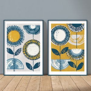 May include: Two framed prints with abstract floral designs. The print on the left has a light gray background with blue and yellow flowers. The print on the right has a yellow background with blue and white flowers.