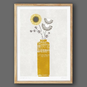 May include: A framed print of a stylized illustration of a yellow vase with a gray and white floral arrangement. The vase has a textured pattern and the flowers are stylized with geometric shapes.