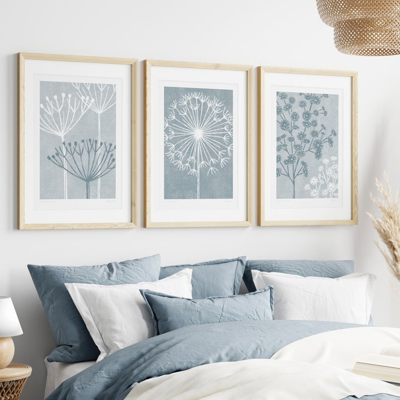 May include: Three framed prints with a blue background and white floral designs. The prints are arranged in a row on a white wall.