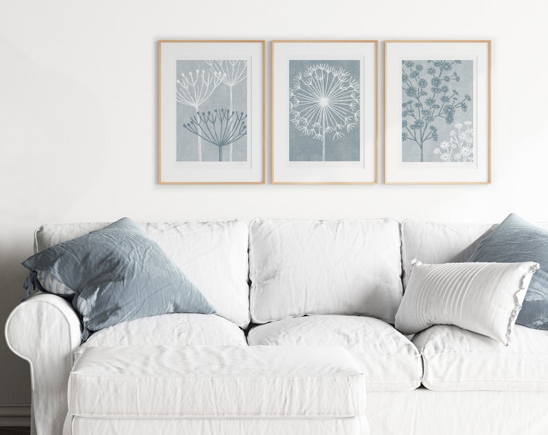May include: Three framed prints with a light blue background and white floral designs. The prints are hanging on a white wall above a white couch with blue throw pillows.