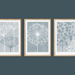 May include: Set of three framed prints featuring stylized illustrations of white flowers on a blue background. The prints are in wooden frames.