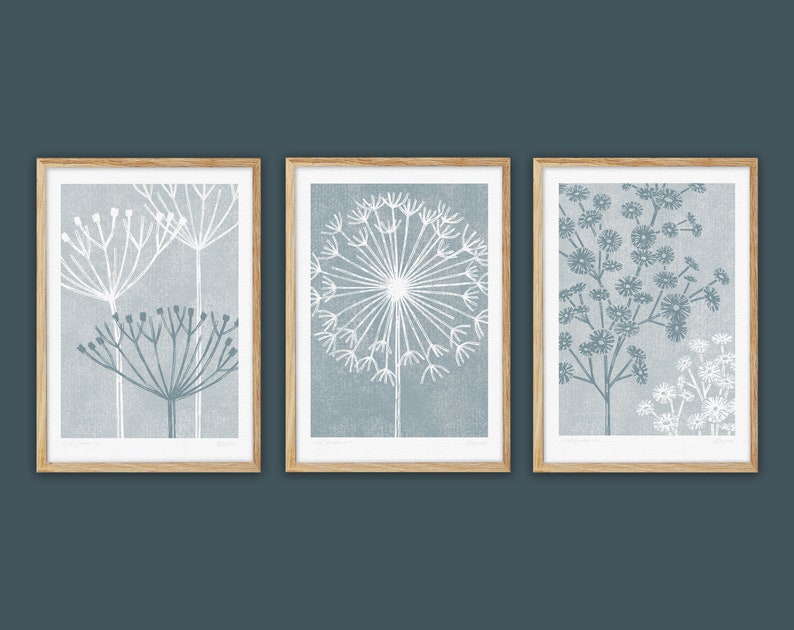 May include: Set of three framed prints featuring stylized illustrations of white flowers on a blue background. The prints are in wooden frames.