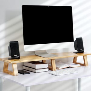 May include: A wooden monitor stand with two shelves, a black computer monitor, two black speakers, a keyboard, and a mobile phone on the bottom shelf.