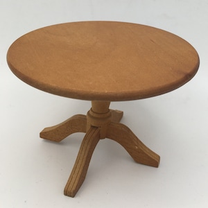 Puede incluir: Una mesa redonda de madera pequeña con un acabado simple y natural. La mesa tiene una base de pedestal con tres patas.