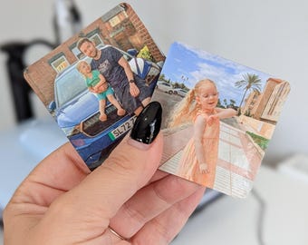 May include: Two square photo prints held in a hand. One shows a man and child by a blue car, the other a girl in a peach dress. The prints are personalized with family photos.