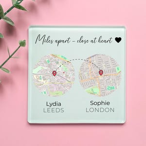 May include: A square glass coaster featuring the text Miles apart - close at heart with a black heart icon. It displays two circular map sections connected by a dashed line, each with a red location pin. Below are the names Lydia, Leeds, Sophie, London.