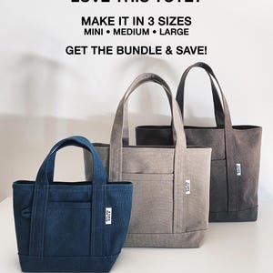 K&ouml;nnte beinhalten: Drei Tragetaschen in den Gr&ouml;&szlig;en Mini, Medium und Large in den Farben Dunkelblau, Hellgrau und Dunkelgrau. Jede Tasche hat zwei Henkel, eine Vordertasche und ein wei&szlig;es Etikett mit der Aufschrift NYLON SMILE. Der Text dar&uuml;ber lautet LOVE THIS TOTE?