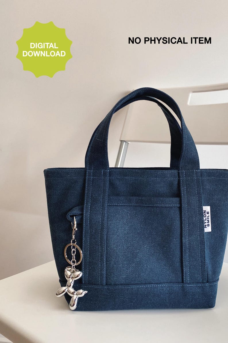 May include: A dark blue canvas tote bag with two top handles, an exterior front pocket, and a silver-toned balloon dog keychain attached to the side. A white rectangular label on the front reads NYLON SMILE. Text reads DIGITAL DOWNLOAD.