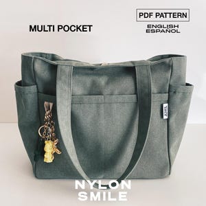 May include: A sage green multi-pocket tote bag with two shoulder straps and a small white brand tag on the side. A gold-toned keychain with a yellow bear charm hangs from the front. Text on the image reads: MULTI POCKET, PDF PATTERN, ENGLISH, ESPAÑOL, NYLON SMILE.
