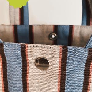 May include: A tote bag featuring vertical stripes in light blue, dark brown, and cream. The bag has a silver metal snap closure and a white rectangular label with the black text NYLON SMILE. A green starburst graphic reads DIGITAL DOWNLOAD and NO PHYSICAL ITEM.