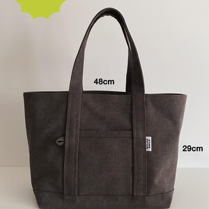 May include: A dark gray canvas tote bag with two shoulder straps, a front pocket, and a small white label reading NYLON SMILE. The bag measures 48 cm in width and 29 cm in height. A lime green starburst graphic in the top left corner reads SKILL LEVEL BEGINNER.