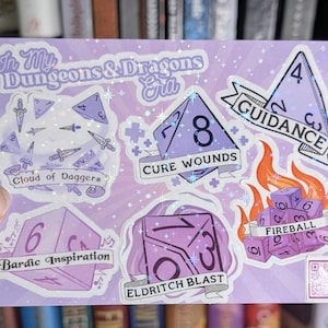 Puede incluir: Un conjunto de 8 pegatinas con temática de Dungeons & Dragons con un acabado holográfico morado y blanco. Las pegatinas presentan varios dados con diferentes números y nombres de hechizos como "Guidance", "Cure Wounds", "Fireball", "Eldritch Blast" y "Bardic Inspiration".