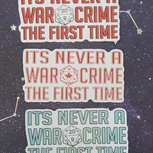 K&ouml;nnte beinhalten: Drei wei&szlig;e Aufkleber mit rotem, wei&szlig;em und blauem Text und einer schwarzen und wei&szlig;en W&uuml;rfelgrafik. Der Text auf den Aufklebern lautet "ITS NEVER A WAR CRIME THE FIRST TIME".