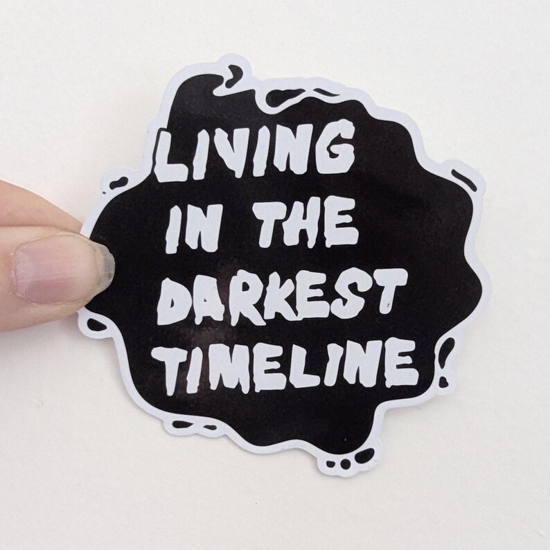 May include: Black and white sticker with the text "Living in the darkest timeline".