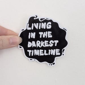 May include: Black and white sticker with the text "Living in the darkest timeline".