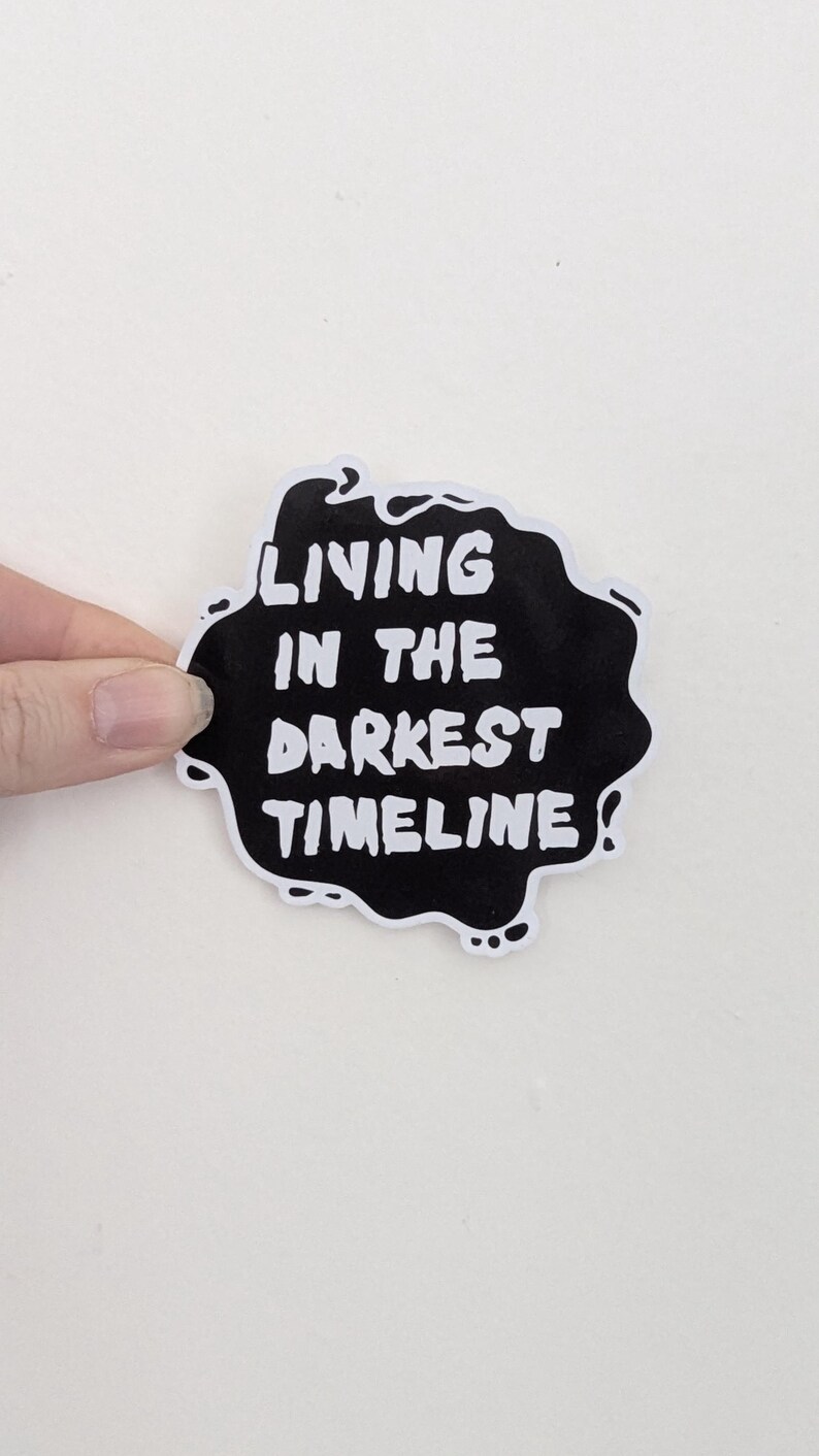 May include: Black and white sticker with the text "Living in the darkest timeline".