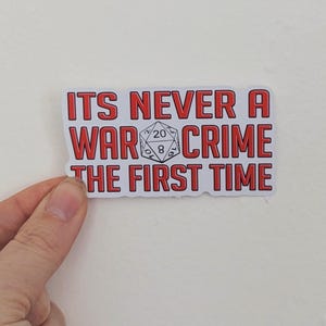 K&ouml;nnte beinhalten: Roter und wei&szlig;er Aufkleber mit dem Text "ITS NEVER A WAR CRIME THE FIRST TIME" und einer Schwarzwei&szlig;illustration eines 20-seitigen W&uuml;rfels.