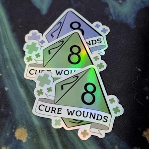 May include: Three iridescent stickers featuring a green d8 die with the text "Cure Wounds" on a banner. The die shows a result of 8.