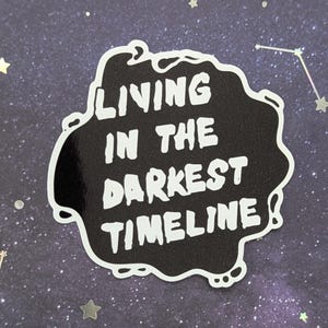 May include: Black and white sticker with a white outline in the shape of a cloud. The sticker says "Living in the darkest timeline".