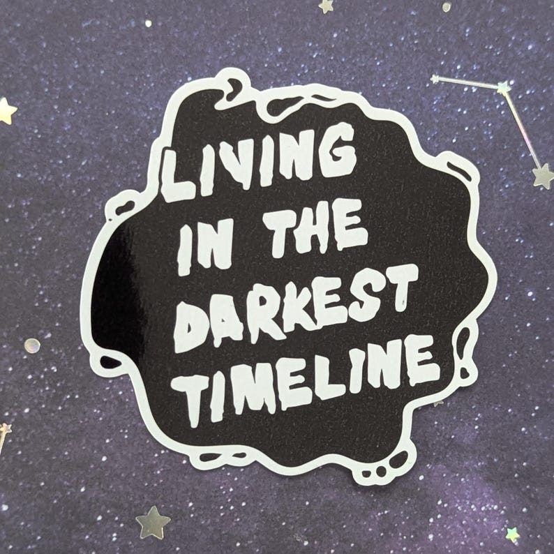 May include: Black and white sticker with a white outline in the shape of a cloud. The sticker says "Living in the darkest timeline".