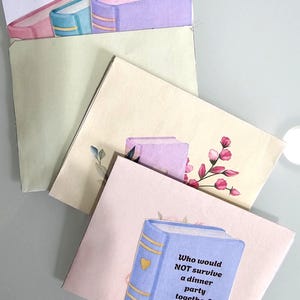 Peut inclure: Ensemble de trois cartes de v&oelig;ux d&eacute;coratives avec des illustrations de livres. La carte du haut pr&eacute;sente une pile de livres roses, bleus et violets. La carte du bas a un livre bleu avec le texte : "Qui ne survivrait PAS &agrave; un d&icirc;ner ensemble ?"