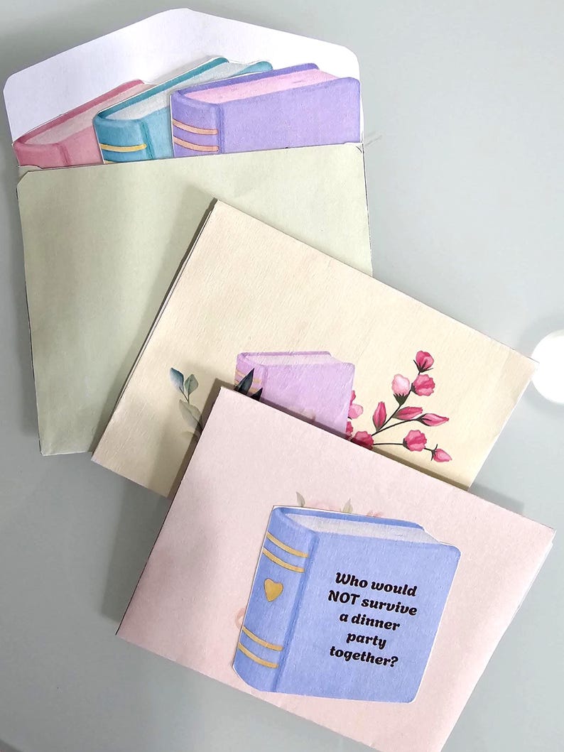Peut inclure: Ensemble de trois cartes de v&oelig;ux d&eacute;coratives avec des illustrations de livres. La carte du haut pr&eacute;sente une pile de livres roses, bleus et violets. La carte du bas a un livre bleu avec le texte : "Qui ne survivrait PAS &agrave; un d&icirc;ner ensemble ?"