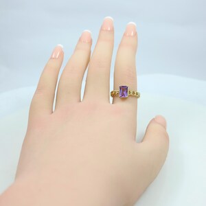 May include: A gold ring with a rectangular purple gemstone. The ring features a chain-link design around the band. The gemstone is a vibrant purple color, set in a gold bezel.