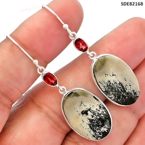 Può includere: Orecchini pendenti in argento con pietre di pirite ovali con inclusioni nere e piccole pietre rosse. Gli orecchini hanno un design semplice con chiusura a gancio. Gli orecchini sono mostrati su uno sfondo neutro.