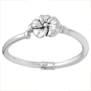 May include: A silver-colored ring featuring a detailed flower design at the center. The ring's band is a smooth, continuous loop, with a clasp at the bottom. The flower has multiple petals and a textured center, creating a three-dimensional effect.