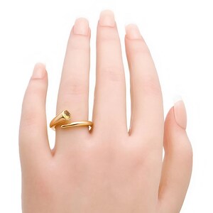 May include: A gold-colored ring with a spiral design and a yellow gemstone. The ring is worn on a finger, showcasing its elegant and modern style. The gemstone is round and set in a prong setting, adding a touch of sparkle.