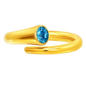 May include: A gold-colored ring with a bright blue oval gemstone. The ring has a smooth, polished finish and a unique, open design. The gemstone is set in a bezel setting, and the ring wraps around the finger.