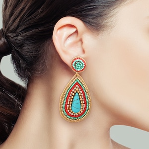 May include: A teardrop-shaped beaded earring featuring a circular stud top. The design incorporates concentric layers of turquoise, red, and metallic gold seed beads surrounding a central smooth turquoise stone with dark veining.