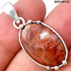 May include: An oval-shaped pendant featuring a polished, mottled reddish-brown stone set in a silver-toned metal frame with small decorative spheres along the edge. The text SDP140715 is visible in the upper right corner of the image.