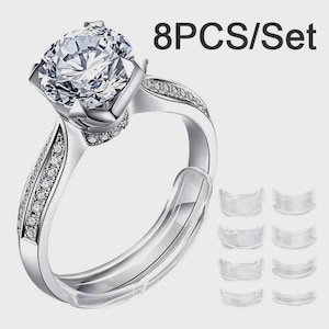 May include: A silver ring featuring a large, clear, round gemstone and smaller accent stones. The image also shows eight clear, curved ring size adjusters. The text "8PCS/Set" is visible in the top right corner.
