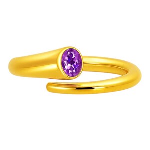 May include: A gold-colored ring with a purple oval gemstone. The ring has a modern, open design, with the gemstone set in a bezel setting. The band curves around the finger, creating a stylish and elegant look.
