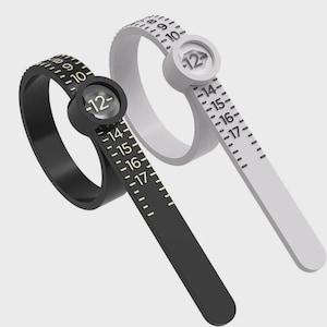 May include: Two ring sizers, one black and one white, with a sliding band and numbered scale. Each sizer has a circular dial with the number 12. The scales measure ring sizes from 9 to 17.