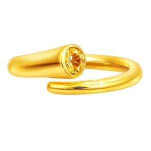 May include: A gold-colored ring with a bright yellow gemstone. The ring has a modern, open design with a rounded band that wraps around the finger. The gemstone is round and set in a bezel setting.