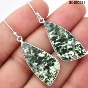 May include: A pair of silver dangle earrings with teardrop-shaped green and white speckled stones. The earrings have a simple hook design and a polished silver frame around the stone. The earrings are shown against a neutral background.