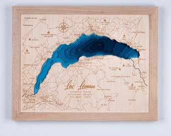 May include: A wooden map of Lake Geneva, also known as Lac Leman, in Switzerland and France. The map is carved in a layered style, with the lake depicted in shades of blue. The surrounding area is shown in a light wood color. The map includes the text "Lac Leman", "Switzerland - France", "Surface area: 224 sq mi", and "Max. depth: 1,020 ft".