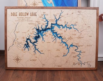 May include: A wooden framed map of Dale Hollow Lake in Tennessee and Kentucky. The lake is depicted in blue, with the surrounding land in a light brown color. The map includes text indicating the lake's maximum depth of 130 feet and surface area of 27,700 acres.