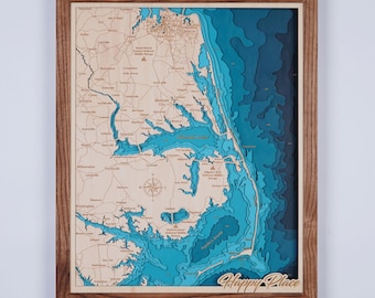 May include: A wooden map of the Outer Banks, North Carolina, with a blue and green layered ocean effect. The map is framed in a dark wood frame and has the words "Happy Place" written in the bottom right corner.